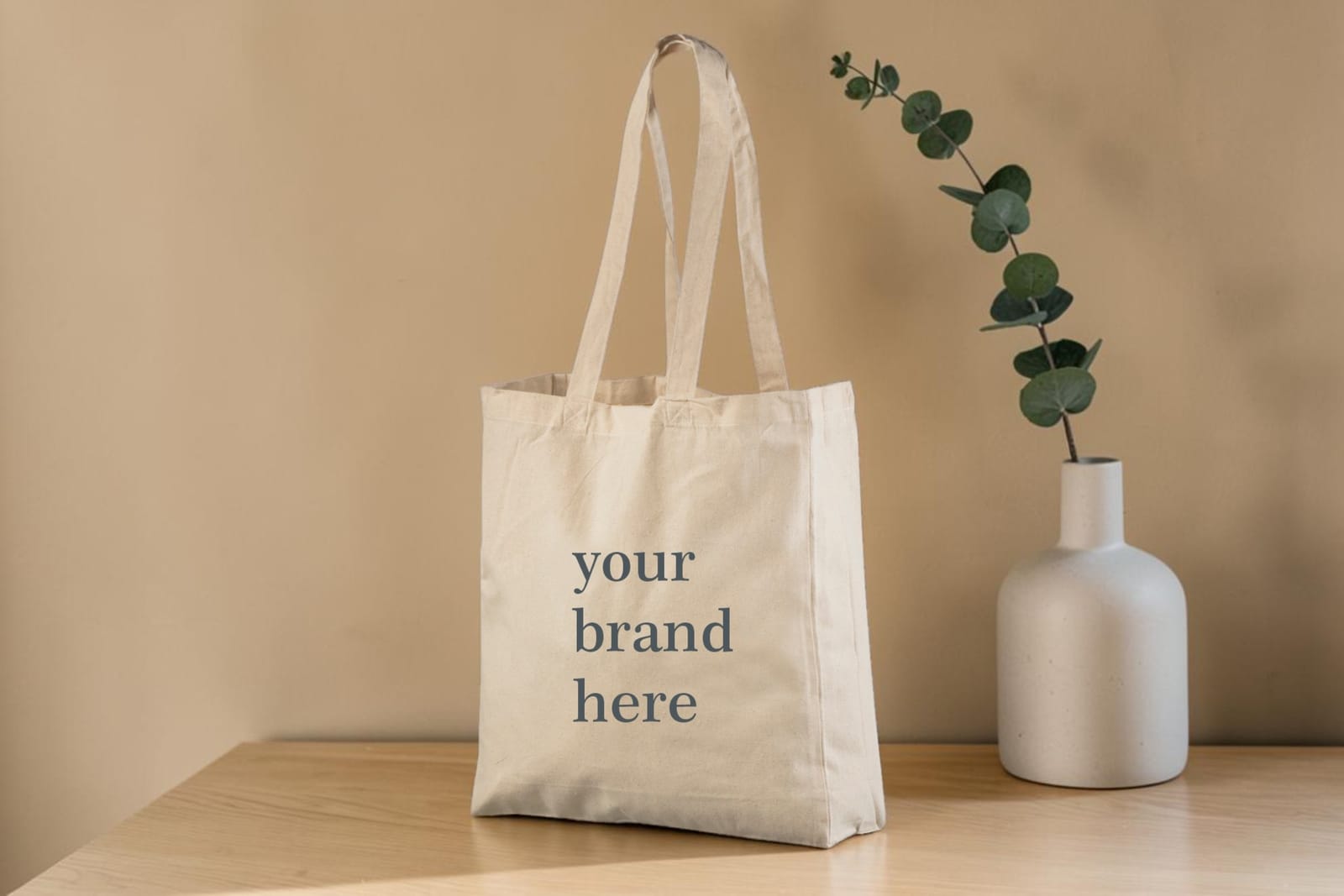 Bomullskasse med tryck – ”your brand here” på en kasse på träbord vid en vit vas – natur.